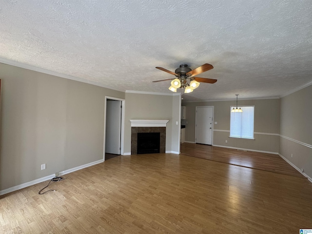 unfurnished living room featuring a tile fireplace, wood finished floors, a ceiling fan, baseboards, and ornamental molding