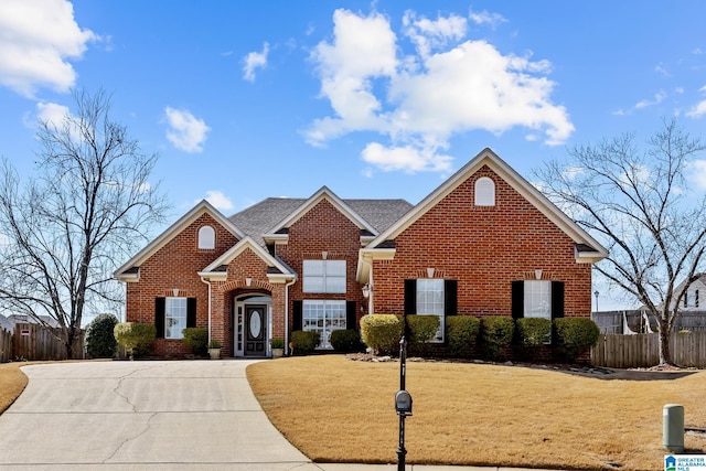 traditional-style home with a shingled roof, brick siding, fence, and a front lawn