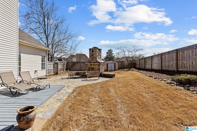 view of yard with an outbuilding, a patio, a storage shed, a stone fireplace, and a fenced backyard