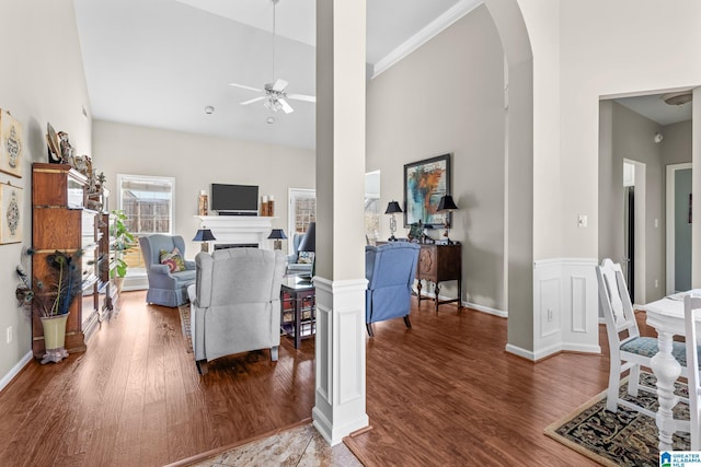 living area with arched walkways, a fireplace, a high ceiling, ceiling fan, and wood finished floors