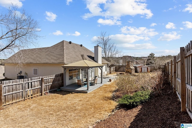 rear view of property featuring an outbuilding, a fenced backyard, a storage shed, a gazebo, and roof with shingles