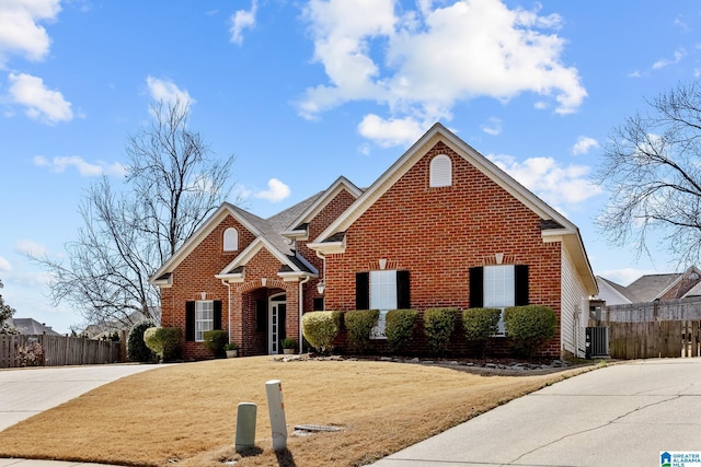 traditional home with central AC unit, concrete driveway, fence, a front lawn, and brick siding