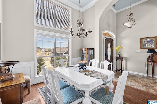 dining area with a towering ceiling, arched walkways, crown molding, and wainscoting