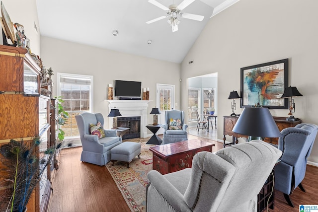 living area with high vaulted ceiling, a fireplace, wood finished floors, and a ceiling fan