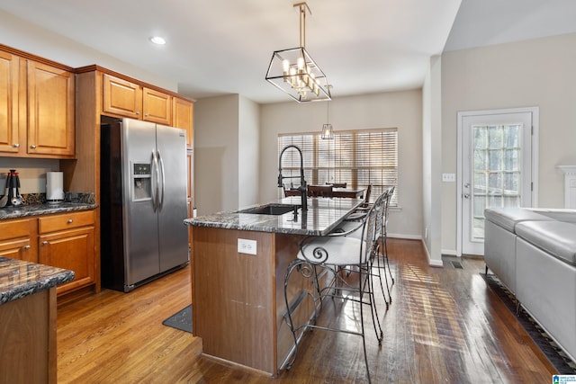 kitchen featuring stainless steel fridge, brown cabinetry, a breakfast bar, wood finished floors, and a sink