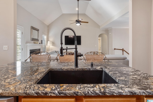 kitchen with a fireplace, open floor plan, vaulted ceiling, a sink, and dark stone countertops