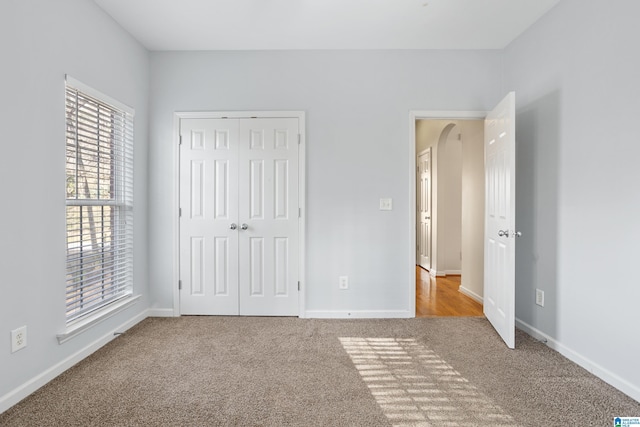 unfurnished bedroom with arched walkways, carpet flooring, and baseboards