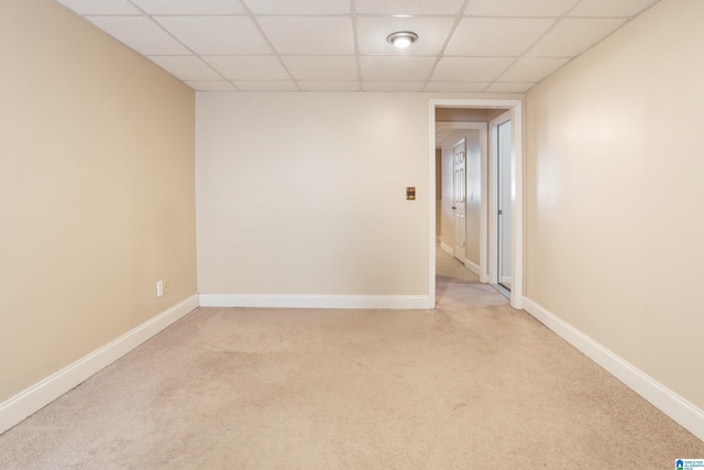 empty room with baseboards, a drop ceiling, and light colored carpet