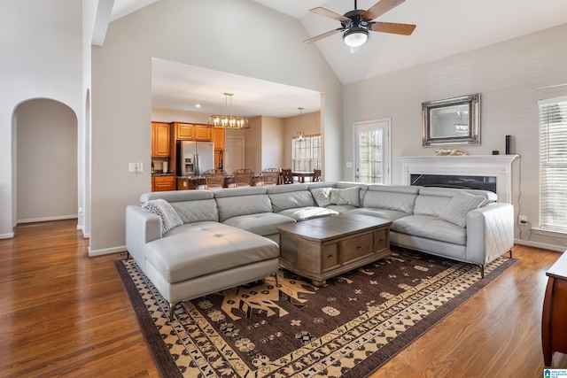 living area with arched walkways, high vaulted ceiling, wood finished floors, and a wealth of natural light