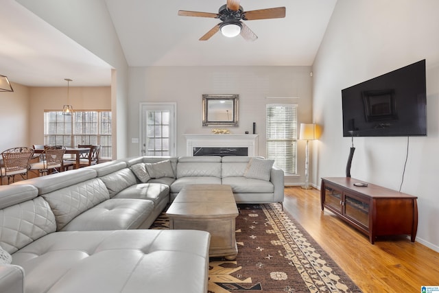 living area featuring baseboards, ceiling fan, vaulted ceiling, light wood-style floors, and a fireplace