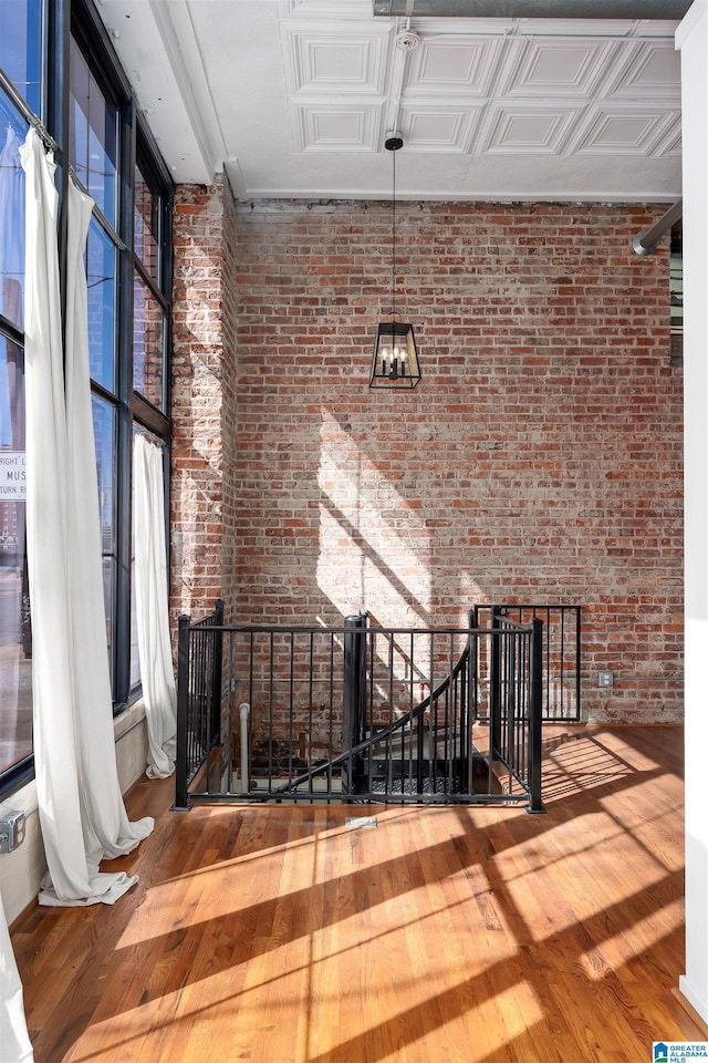 interior space with a wealth of natural light, wood-type flooring, brick wall, and an upstairs landing