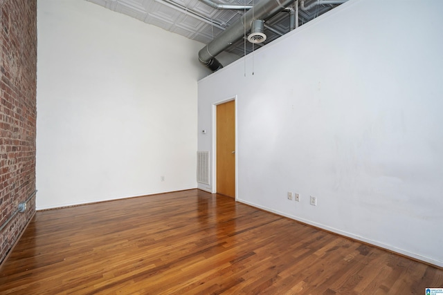 unfurnished room with visible vents, a towering ceiling, brick wall, and wood finished floors