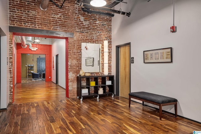 hallway featuring brick wall, wood-type flooring, and a towering ceiling