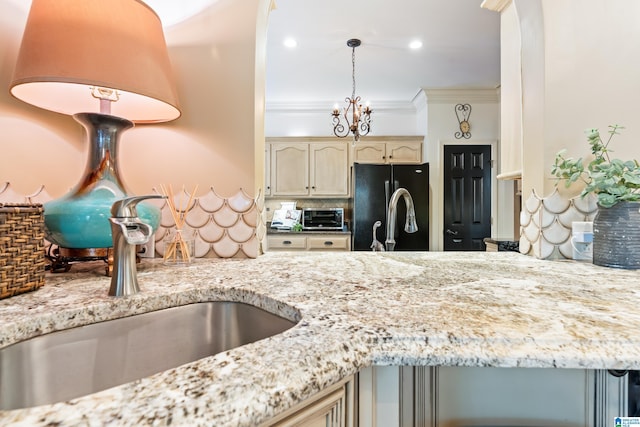 kitchen featuring light stone counters, ornamental molding, freestanding refrigerator, a sink, and backsplash