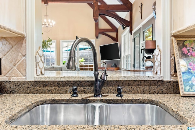 kitchen with light stone counters, a sink, decorative light fixtures, and tasteful backsplash