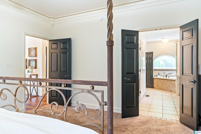 bedroom featuring light tile patterned floors, ornamental molding, connected bathroom, and light colored carpet