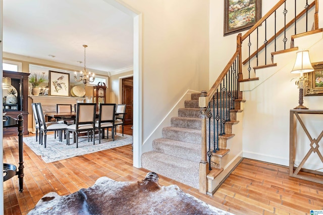 staircase with a chandelier, ornamental molding, wood finished floors, and baseboards