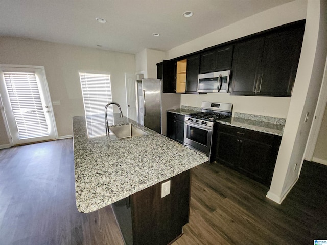 kitchen with dark wood-style flooring, stainless steel appliances, a sink, an island with sink, and dark cabinetry