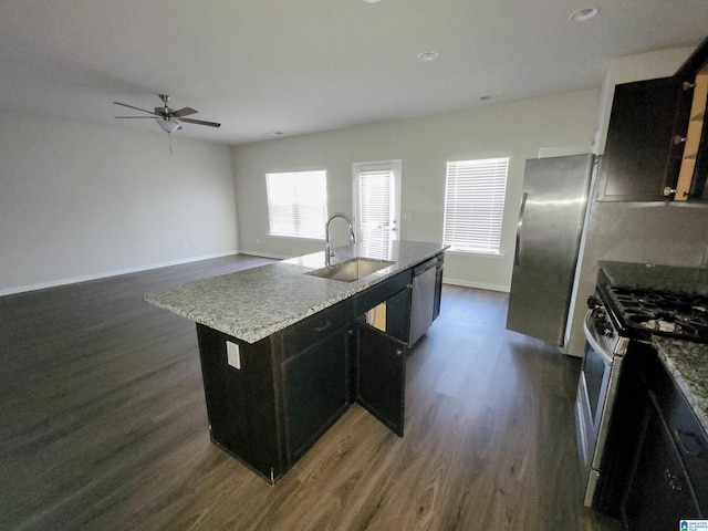 kitchen featuring baseboards, appliances with stainless steel finishes, dark wood-style flooring, a kitchen island with sink, and a sink