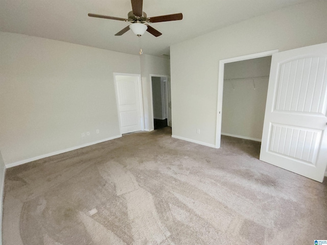 unfurnished bedroom featuring baseboards, a ceiling fan, a walk in closet, carpet floors, and a closet