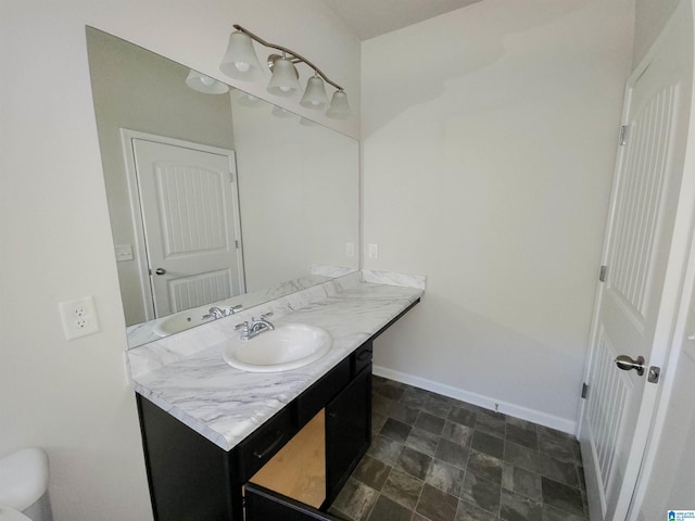 bathroom with toilet, stone finish floor, vanity, and baseboards