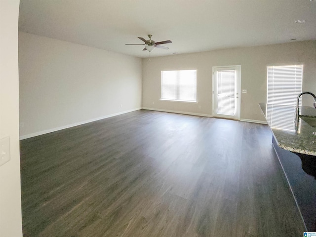 unfurnished living room featuring dark wood-style floors, ceiling fan, and baseboards