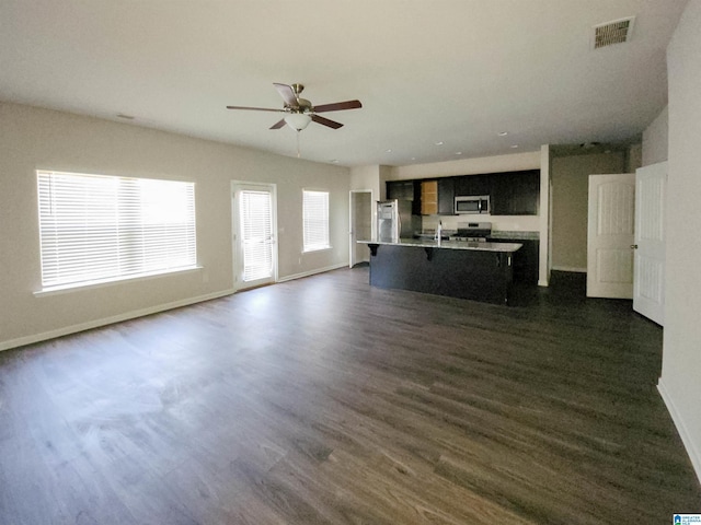 unfurnished living room with dark wood-type flooring, a ceiling fan, visible vents, and baseboards