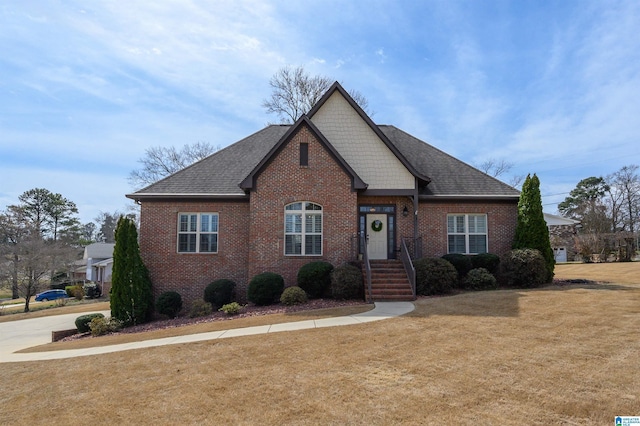 view of front facade featuring a front yard, brick siding, and roof with shingles