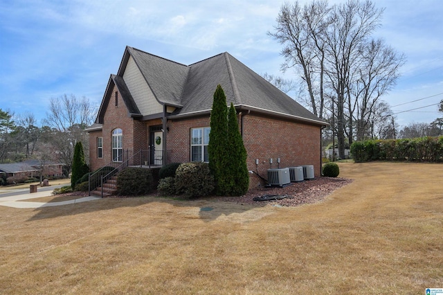 view of home's exterior featuring brick siding, roof with shingles, central AC, and a yard