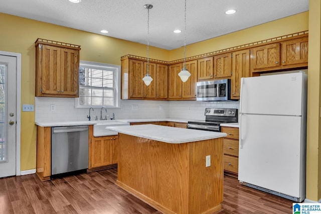 kitchen featuring stainless steel appliances, a sink, light countertops, a center island, and dark wood finished floors