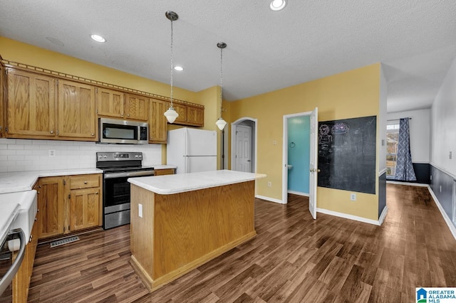 kitchen featuring arched walkways, dark wood finished floors, appliances with stainless steel finishes, a center island, and light countertops