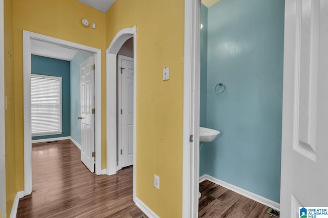 hallway featuring baseboards, visible vents, arched walkways, and wood finished floors