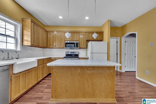 kitchen featuring tasteful backsplash, a kitchen island, appliances with stainless steel finishes, wood finished floors, and a sink