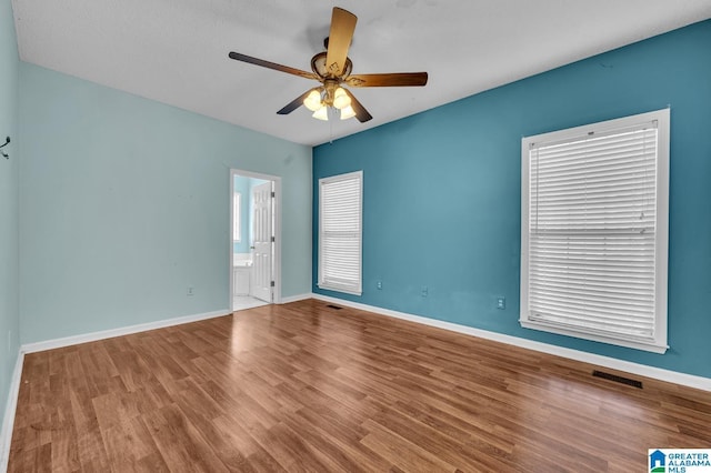 empty room with a ceiling fan, baseboards, visible vents, and wood finished floors