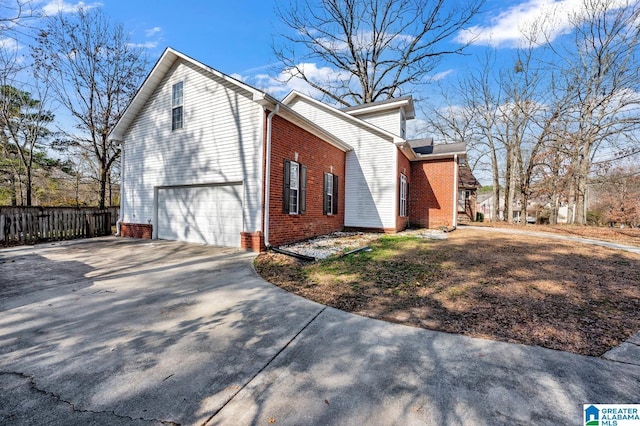 view of side of property featuring driveway, brick siding, an attached garage, and fence