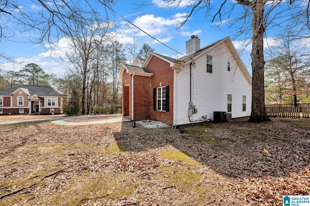 view of home's exterior with central AC, brick siding, a chimney, and fence