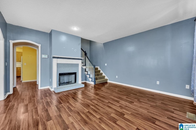 unfurnished living room with baseboards, arched walkways, wood finished floors, stairs, and a fireplace