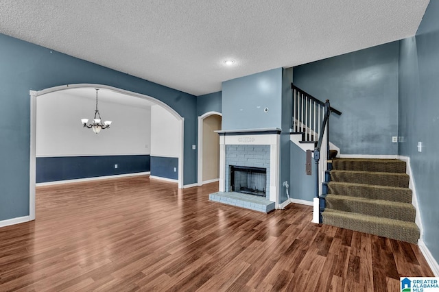 unfurnished living room featuring a brick fireplace, stairway, a chandelier, and wood finished floors