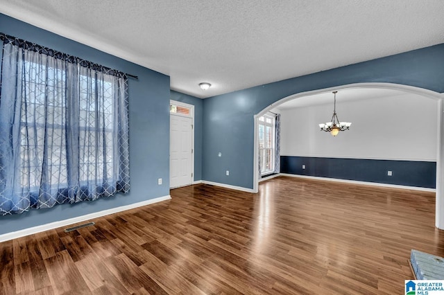 unfurnished living room featuring visible vents, arched walkways, wood finished floors, an inviting chandelier, and a textured ceiling