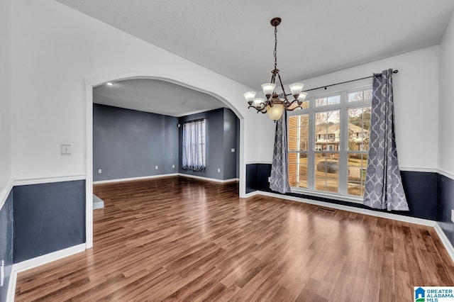 unfurnished dining area featuring a chandelier, arched walkways, baseboards, and wood finished floors