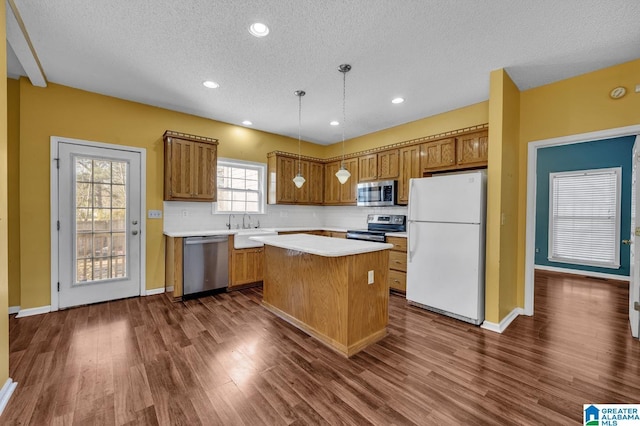 kitchen with brown cabinetry, dark wood-style flooring, a center island, stainless steel appliances, and light countertops