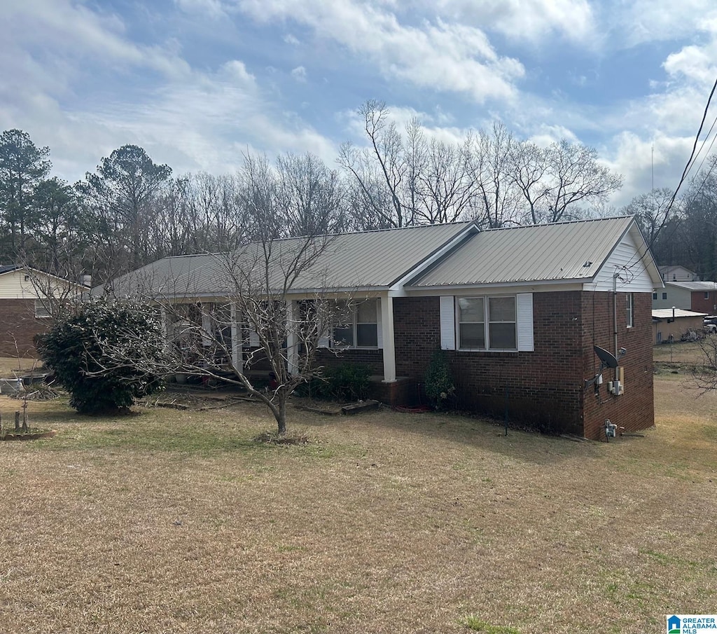 view of front facade with a front yard, brick siding, and metal roof