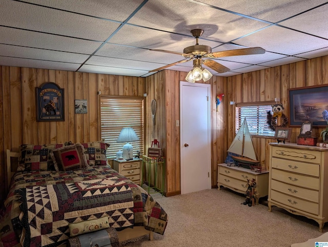 bedroom featuring a ceiling fan, wood walls, a paneled ceiling, and light colored carpet