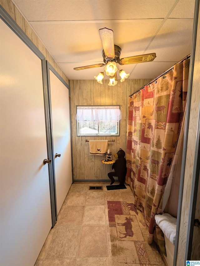 doorway with a ceiling fan, visible vents, and wooden walls