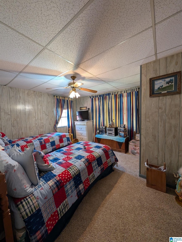 carpeted bedroom featuring a ceiling fan, a paneled ceiling, and wooden walls