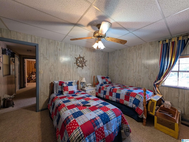 carpeted bedroom with a ceiling fan, a drop ceiling, and wooden walls