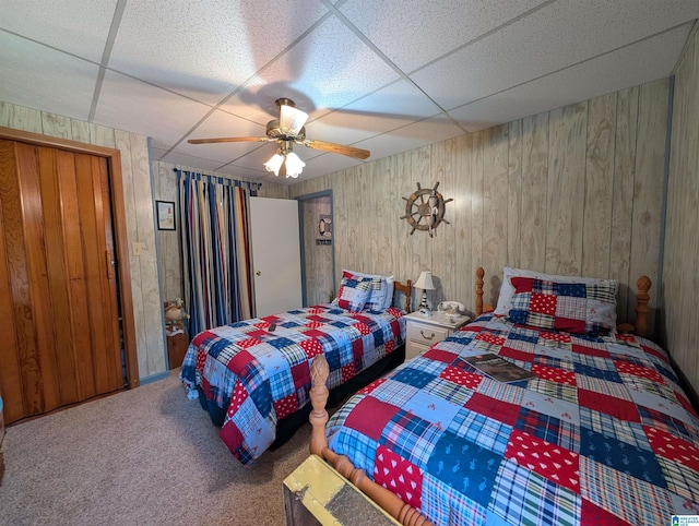 bedroom featuring carpet, wooden walls, ceiling fan, and a drop ceiling