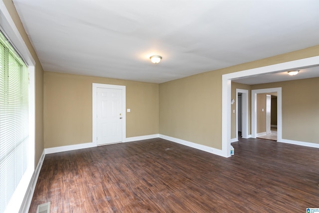 empty room with dark wood-style flooring, visible vents, and baseboards