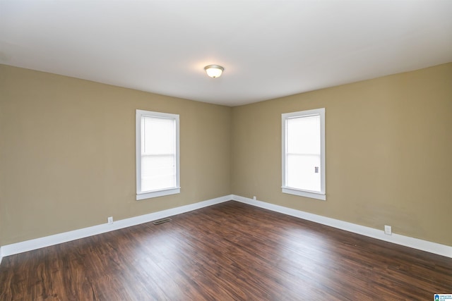 spare room featuring a healthy amount of sunlight, visible vents, baseboards, and dark wood-type flooring