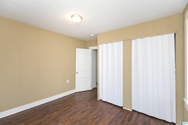 unfurnished bedroom featuring a closet, dark wood finished floors, and baseboards